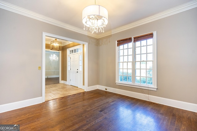 spare room featuring wood finished floors, crown molding, baseboards, and an inviting chandelier