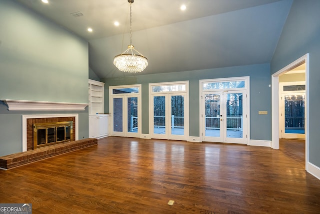 unfurnished living room featuring a brick fireplace, french doors, an inviting chandelier, and wood finished floors