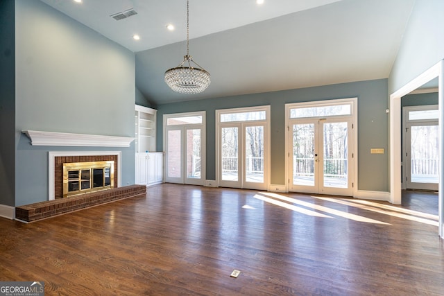 unfurnished living room with built in features, french doors, visible vents, a brick fireplace, and wood finished floors