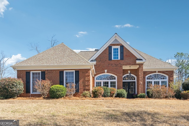 traditional home with roof with shingles, a front yard, and brick siding