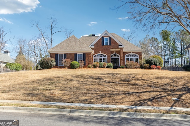 view of front of home with a shingled roof, a chimney, fence, a front lawn, and brick siding