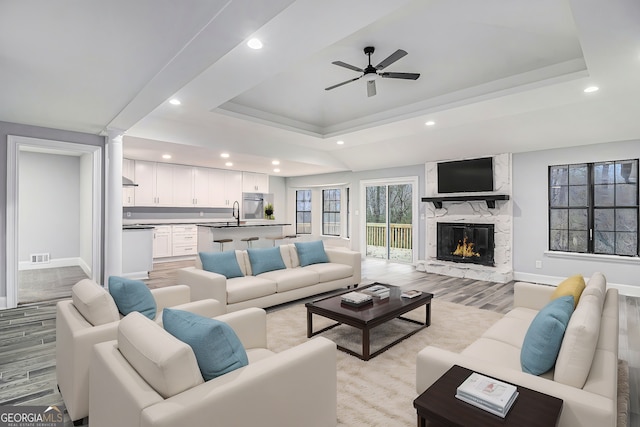 living area with a high end fireplace, a tray ceiling, visible vents, and light wood-style floors