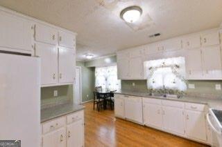 kitchen with a sink, white cabinetry, range, freestanding refrigerator, and light wood finished floors