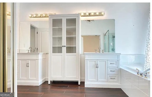 bathroom featuring a shower stall, a bathtub, two vanities, and wood finished floors