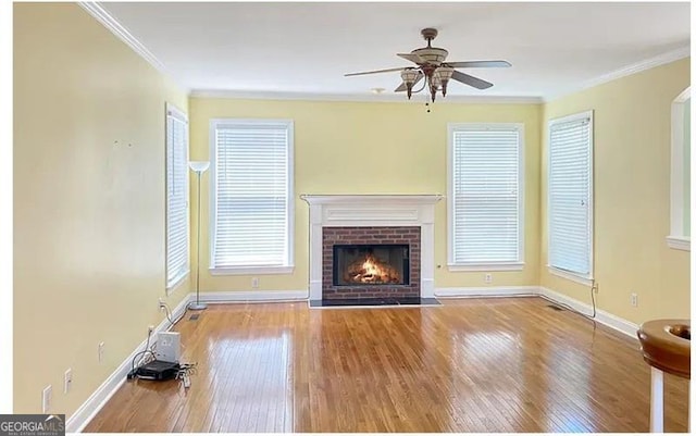 unfurnished living room with a brick fireplace, crown molding, baseboards, and wood finished floors