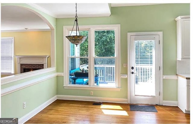 doorway featuring ornamental molding, a brick fireplace, wood finished floors, and baseboards