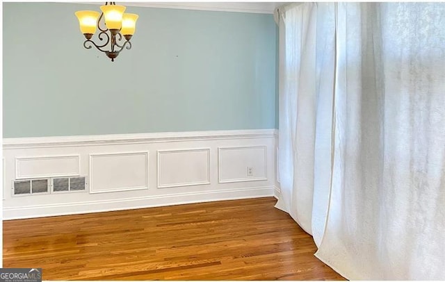 unfurnished dining area with a wainscoted wall, visible vents, an inviting chandelier, and wood finished floors