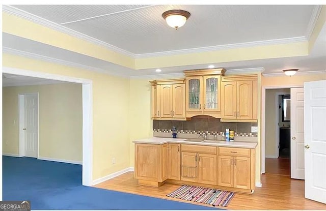 kitchen with a sink, light countertops, tasteful backsplash, a raised ceiling, and glass insert cabinets