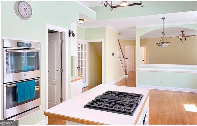 kitchen featuring black gas cooktop, double oven, light wood-style flooring, hanging light fixtures, and crown molding