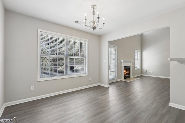 unfurnished living room with a warm lit fireplace, baseboards, a chandelier, and dark wood-type flooring