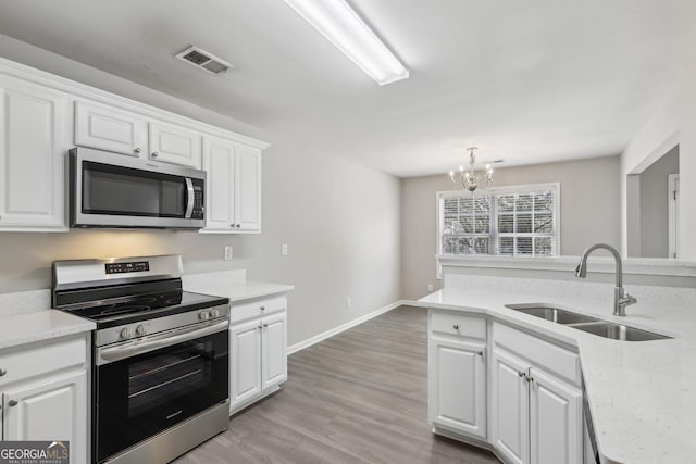 kitchen featuring light wood finished floors, stainless steel appliances, visible vents, white cabinetry, and a sink