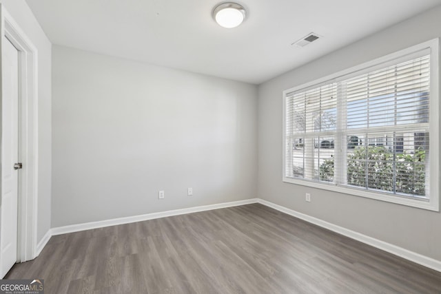 unfurnished room with dark wood-type flooring, visible vents, and baseboards