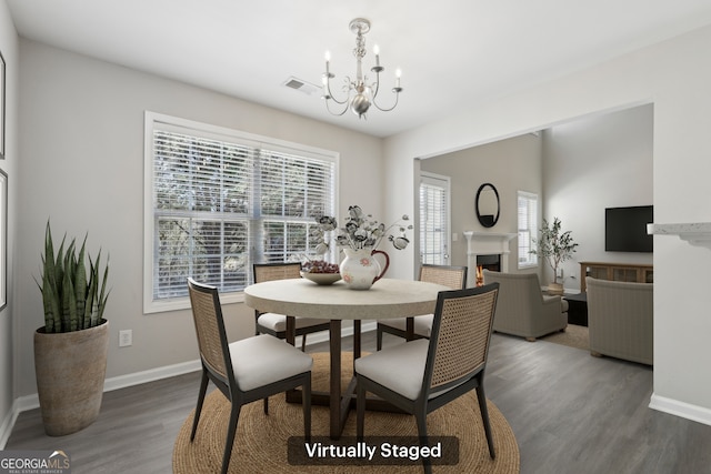 dining area with a warm lit fireplace, a notable chandelier, wood finished floors, visible vents, and baseboards