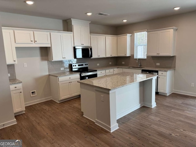 kitchen with appliances with stainless steel finishes, white cabinets, a sink, and a center island