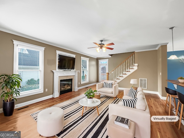 living room with visible vents, a glass covered fireplace, wood finished floors, and ornamental molding