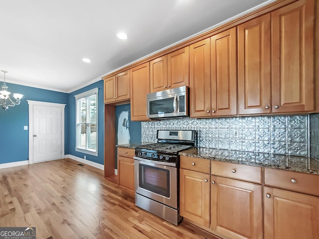 kitchen with light wood finished floors, stainless steel appliances, decorative backsplash, an inviting chandelier, and dark stone counters