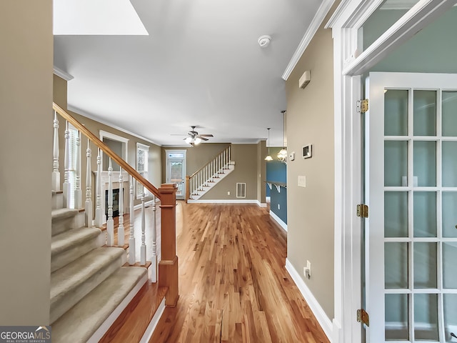 interior space with a ceiling fan, baseboards, ornamental molding, stairway, and light wood finished floors