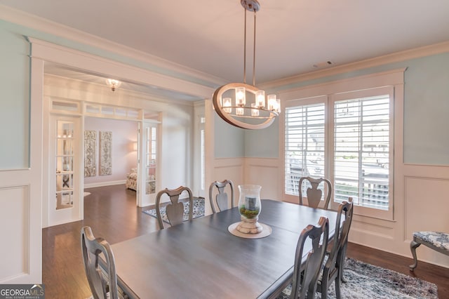 dining area featuring dark wood finished floors, a wainscoted wall, crown molding, a decorative wall, and a notable chandelier