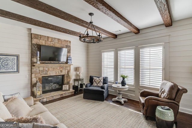 living area featuring wooden walls, visible vents, wood finished floors, a fireplace, and beam ceiling