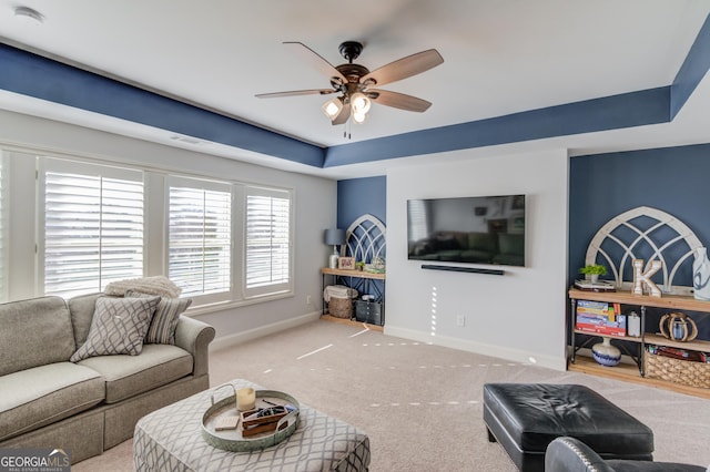 carpeted living area with a ceiling fan, a raised ceiling, and baseboards