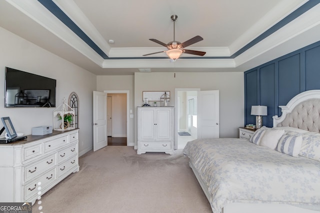 bedroom featuring a tray ceiling, light carpet, crown molding, and a decorative wall