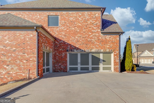 back of house with brick siding, driveway, an attached garage, and roof with shingles