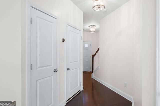 hallway featuring stairs, dark wood-type flooring, and baseboards