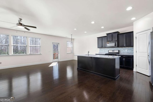 kitchen with a sink, open floor plan, appliances with stainless steel finishes, backsplash, and dark wood-style floors