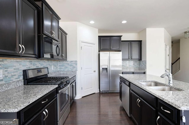 kitchen with dark wood finished floors, appliances with stainless steel finishes, a sink, light stone countertops, and dark cabinets