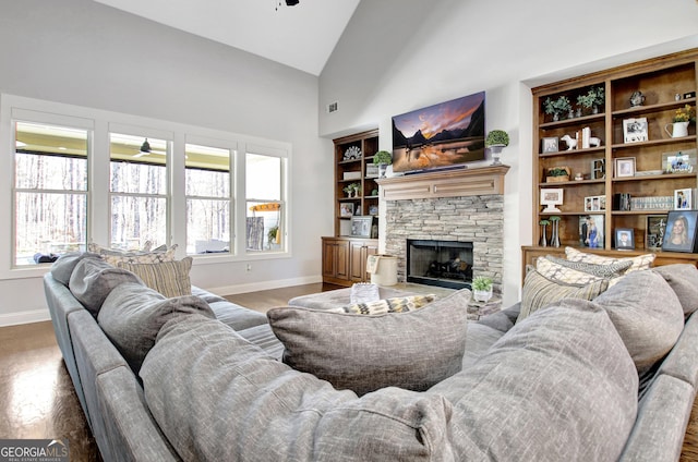 living area with baseboards, ceiling fan, wood finished floors, a fireplace, and high vaulted ceiling