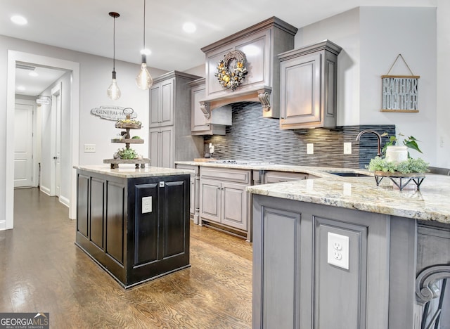 kitchen with decorative light fixtures, backsplash, gray cabinetry, a sink, and wood finished floors