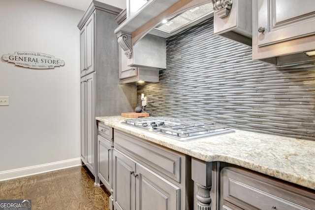 kitchen with light stone counters, dark wood-style flooring, stainless steel gas cooktop, tasteful backsplash, and baseboards