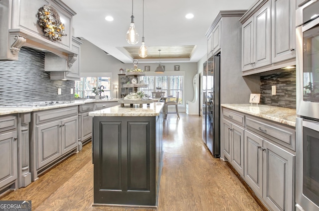 kitchen with a tray ceiling, light wood finished floors, gray cabinets, stovetop, and a peninsula