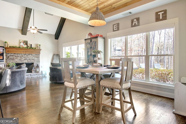 dining space featuring dark wood-style flooring, vaulted ceiling with beams, wood ceiling, a stone fireplace, and baseboards