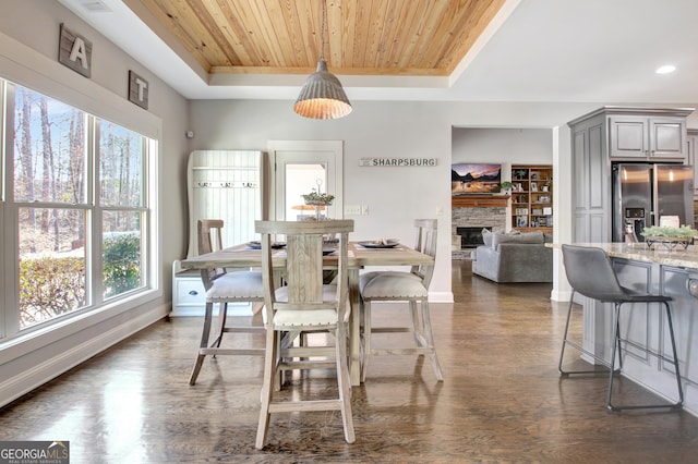 dining room featuring wooden ceiling, a tray ceiling, dark wood finished floors, and a stone fireplace