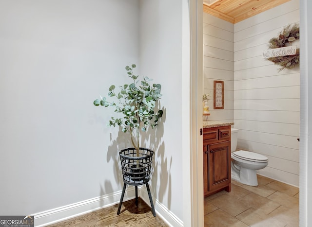 bathroom featuring wood walls, vanity, toilet, and baseboards