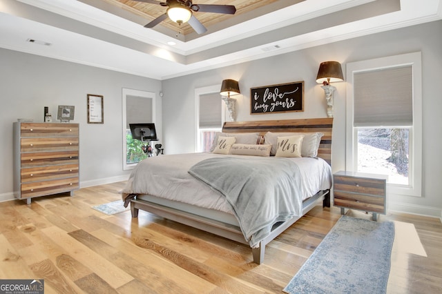 bedroom featuring crown molding, a raised ceiling, visible vents, and light wood-style floors