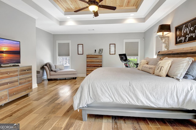 bedroom featuring a tray ceiling, crown molding, baseboards, and wood finished floors