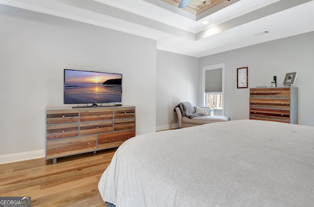 bedroom featuring visible vents, baseboards, light wood-style floors, a raised ceiling, and crown molding