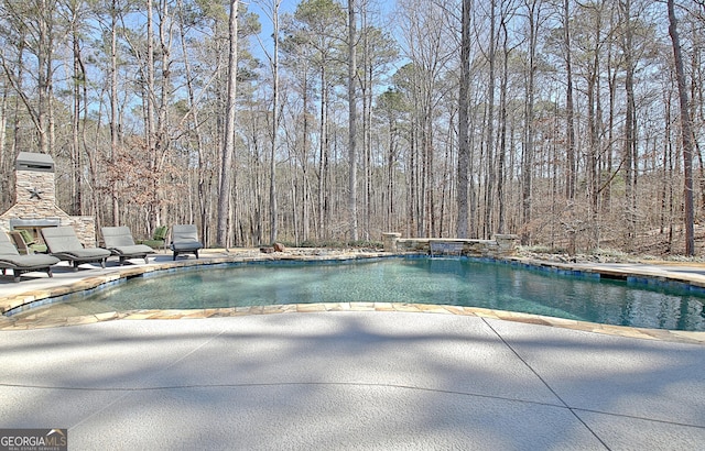 view of swimming pool featuring a pool, a patio area, a fireplace, and a forest view