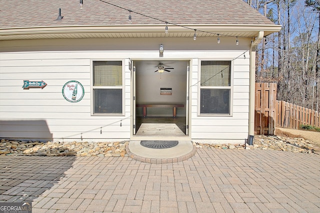 doorway to property with a shingled roof, a patio area, and fence