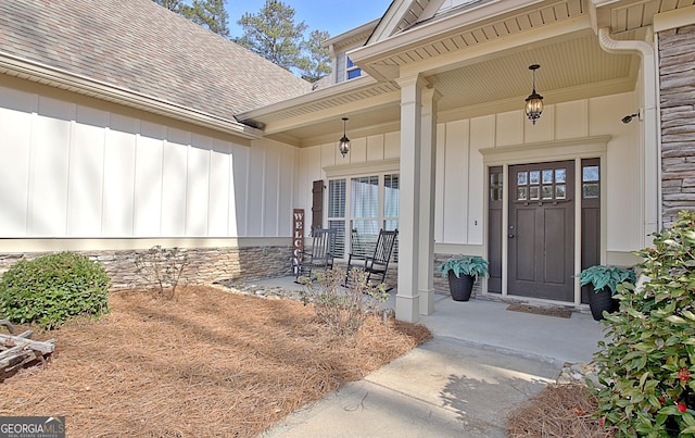 view of exterior entry with board and batten siding, stone siding, a porch, and a shingled roof