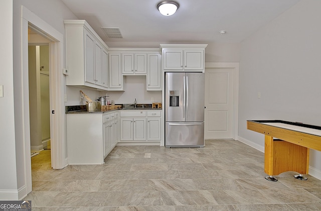 kitchen featuring visible vents, dark countertops, white cabinetry, stainless steel refrigerator with ice dispenser, and a sink