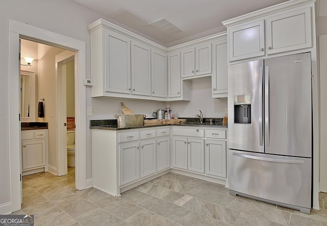 kitchen with visible vents, white cabinets, stainless steel fridge with ice dispenser, dark stone countertops, and a sink