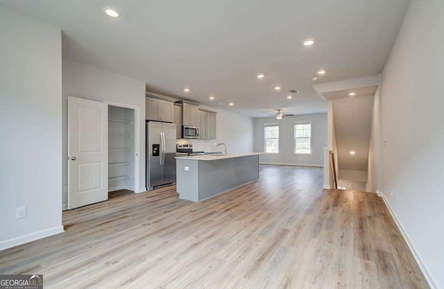 kitchen featuring open floor plan, light countertops, gray cabinetry, a center island with sink, and stainless steel appliances