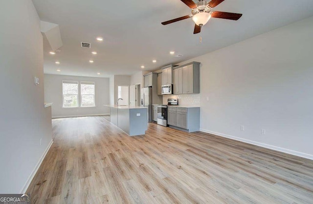 kitchen with visible vents, gray cabinets, a kitchen island with sink, stainless steel appliances, and light wood finished floors