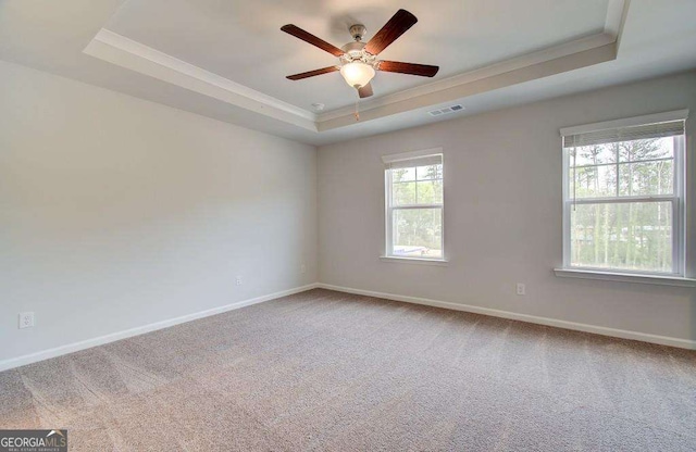carpeted spare room with baseboards, ornamental molding, a raised ceiling, visible vents, and ceiling fan