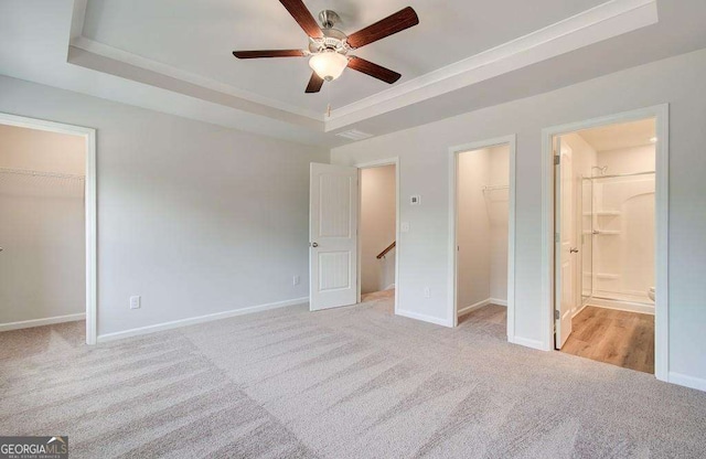 unfurnished bedroom featuring a closet, baseboards, a tray ceiling, a walk in closet, and light carpet