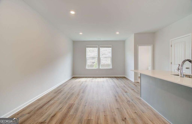 unfurnished living room with light wood-type flooring, a sink, baseboards, and recessed lighting