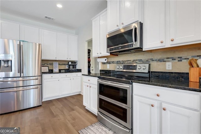 kitchen with stainless steel appliances, wood finished floors, visible vents, white cabinetry, and backsplash